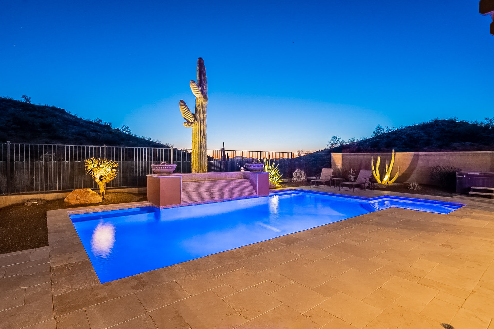 Lit backyard pool at dusk with saguaro cactus and desert hillside